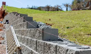 Budowa taniego murku oporowego z bloczków betonowych. Widać drabinę i sznur geodezyjny.