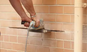 Ręce trzymają szlifierkę kątową, która przecina ceglaną ścianę. Prace remontowe przy nadprożu stalowym.