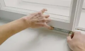 Ręce mierzą długość porysowanego parapetu z blachy przy oknie.
