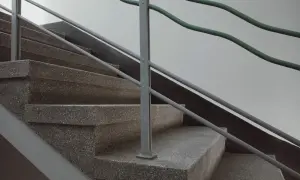 Schody z lastryko, szara poręcz i zielone, faliste pręty.