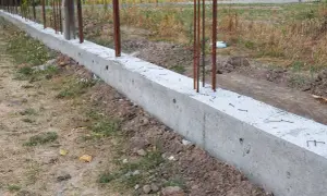 Solidny fundament pod ogrodzenie, z wystającymi prętami zbrojeniowymi, czeka na dalsze prace budowlane.