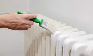 Ręka maluje białą farbą grzejnik. Zastanawiasz się, jaka farba do grzejników będzie najlepsza?