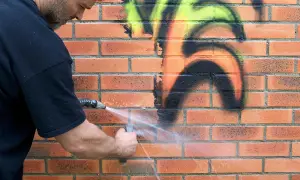 Mężczyzna zmywa graffiti z ceglanej ściany wodą. Dzięki powłoce antygraffiti czyszczenie jest łatwiejsze.