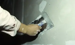 Ręka nakłada gładź gipsową na ścianę za pomocą kielni.
