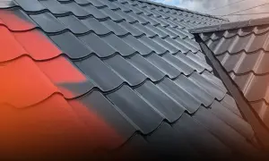 Malowanie blachodachówki na czarno, z widocznym fragmentem czerwonej farby.