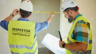 Dwóch inspektorów w kaskach i kamizelkach mierzy pomieszczenie taśmą, jeden trzyma plany.