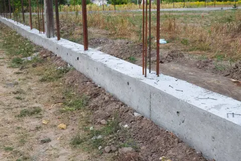 Solidny fundament pod ogrodzenie, z wystającymi prętami zbrojeniowymi, czeka na dalsze prace budowlane.