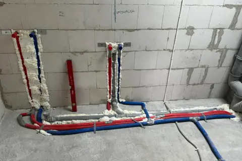 Instalacja wodna z rurami w kolorach czerwonym i niebieskim, izolowana pianką. Widoczna też szara rura kanalizacyjna.