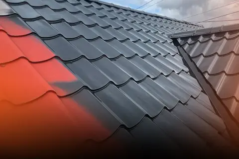 Malowanie blachodachówki na czarno, z widocznym fragmentem czerwonej farby.