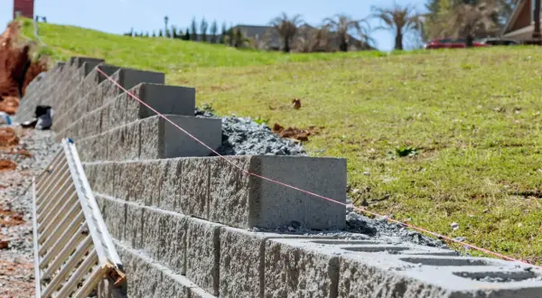 Budowa taniego murku oporowego z bloczków betonowych. Widać drabinę i sznur geodezyjny.