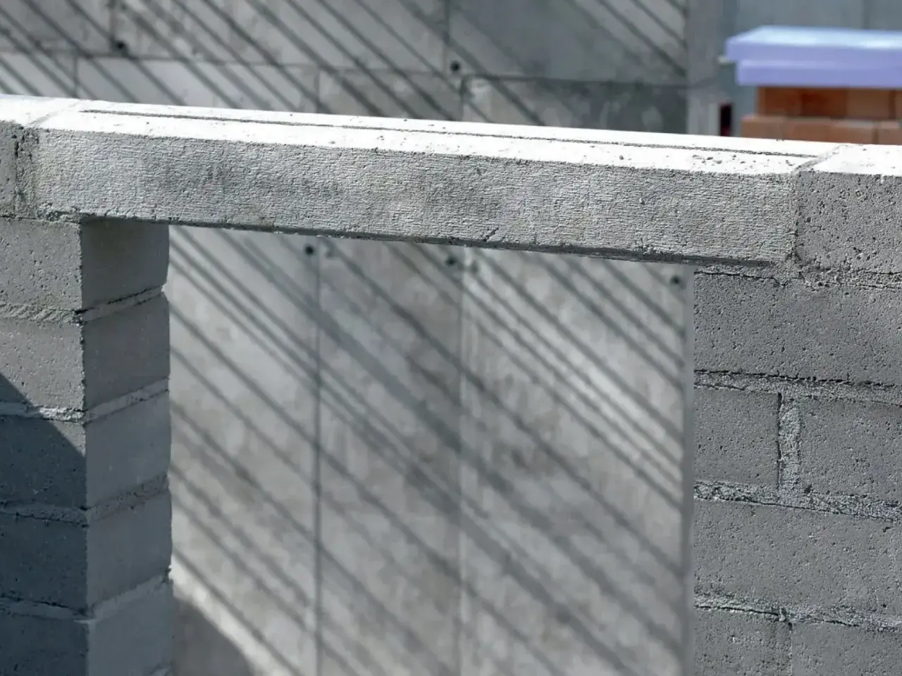 Betonowe nadproże nad otworem w budowie. Cienie ukośnie padają na ścianę z bloczków.