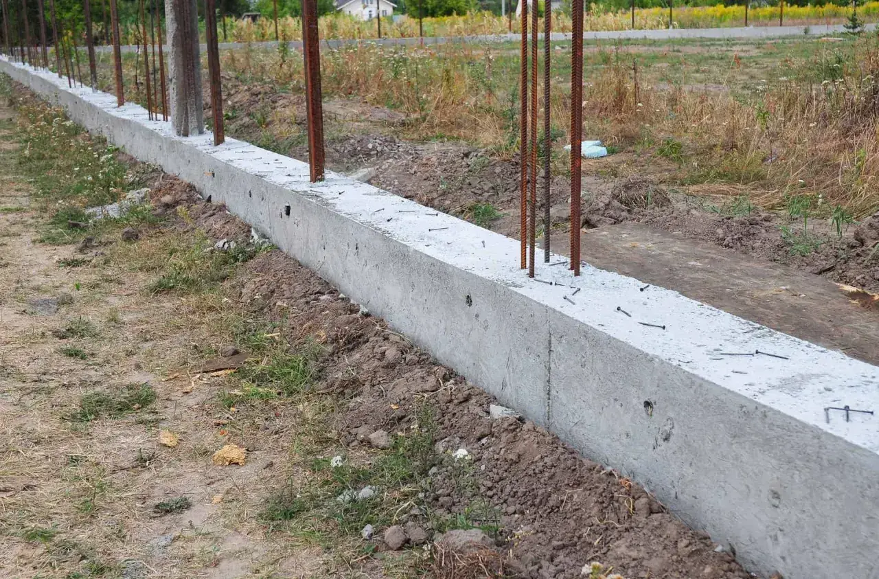 Solidny fundament pod ogrodzenie, z wystającymi prętami zbrojeniowymi, czeka na dalsze prace budowlane.